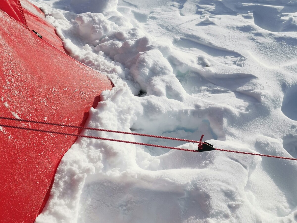 Der untere Rand vom Zelt wird mit etwas Schnee abgedichtet (Foto: Malte Hübner)